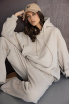 אישה לובשת סט טרנינג בז' עם קפוצ'ון וכובע מצחייה, לוק קז'ואל אופנתי לנשים