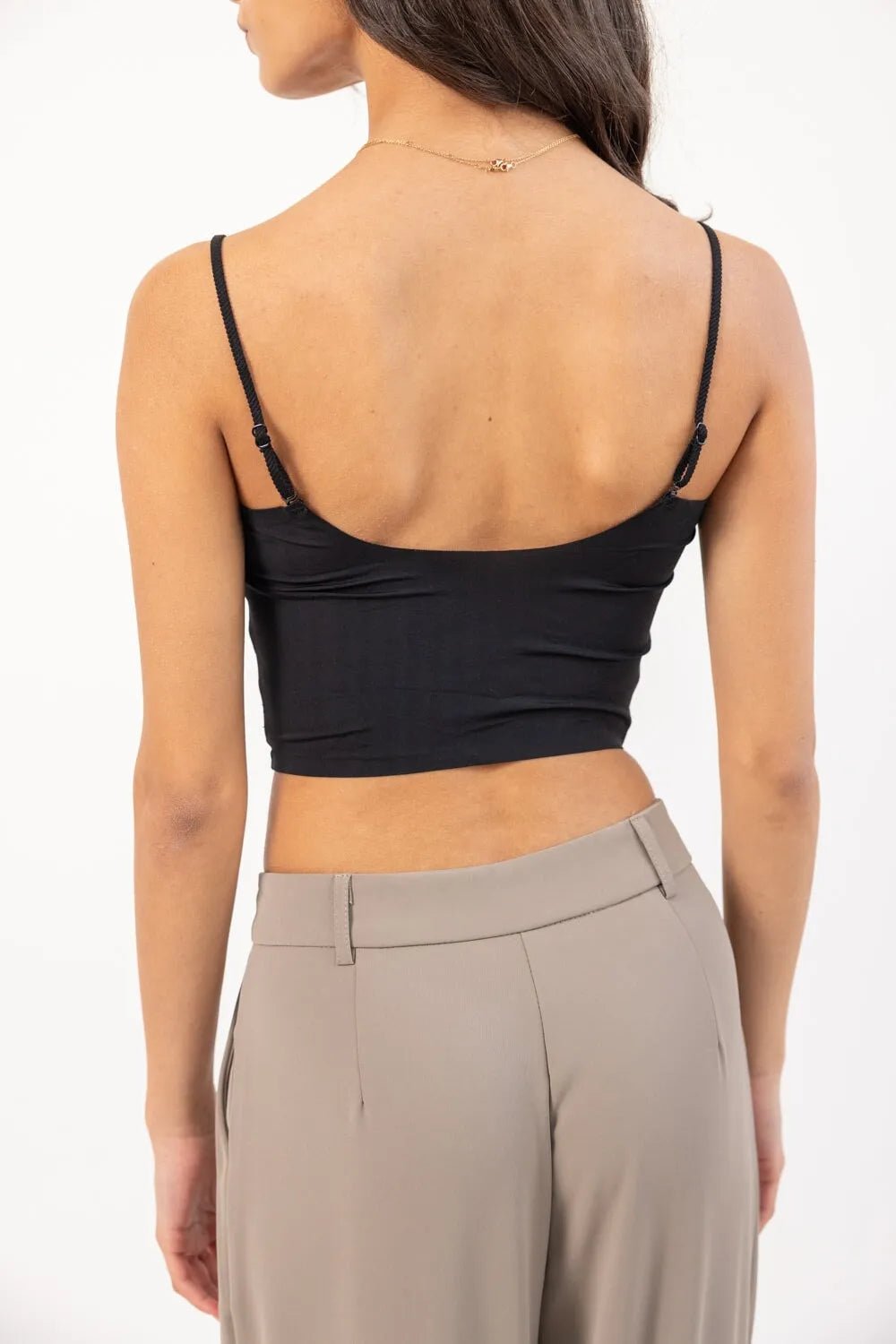 אישה לובשת טופ שחור קצר עם כתפיות דקיקות ומכנסיים מחויטים בצבע בז'