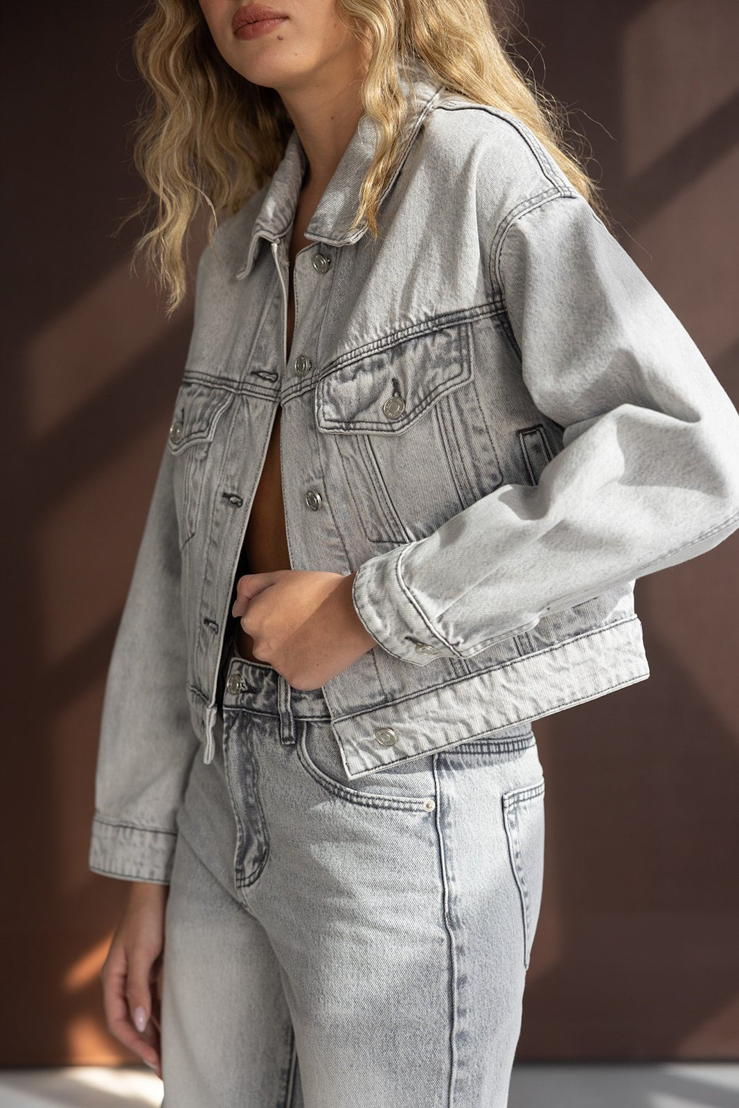 דוגמנית לובשת ג'קט ג'ינס קצר ואופנתי עם מכנסי ג'ינס תואמים בגוון אפור בהיר לנשים