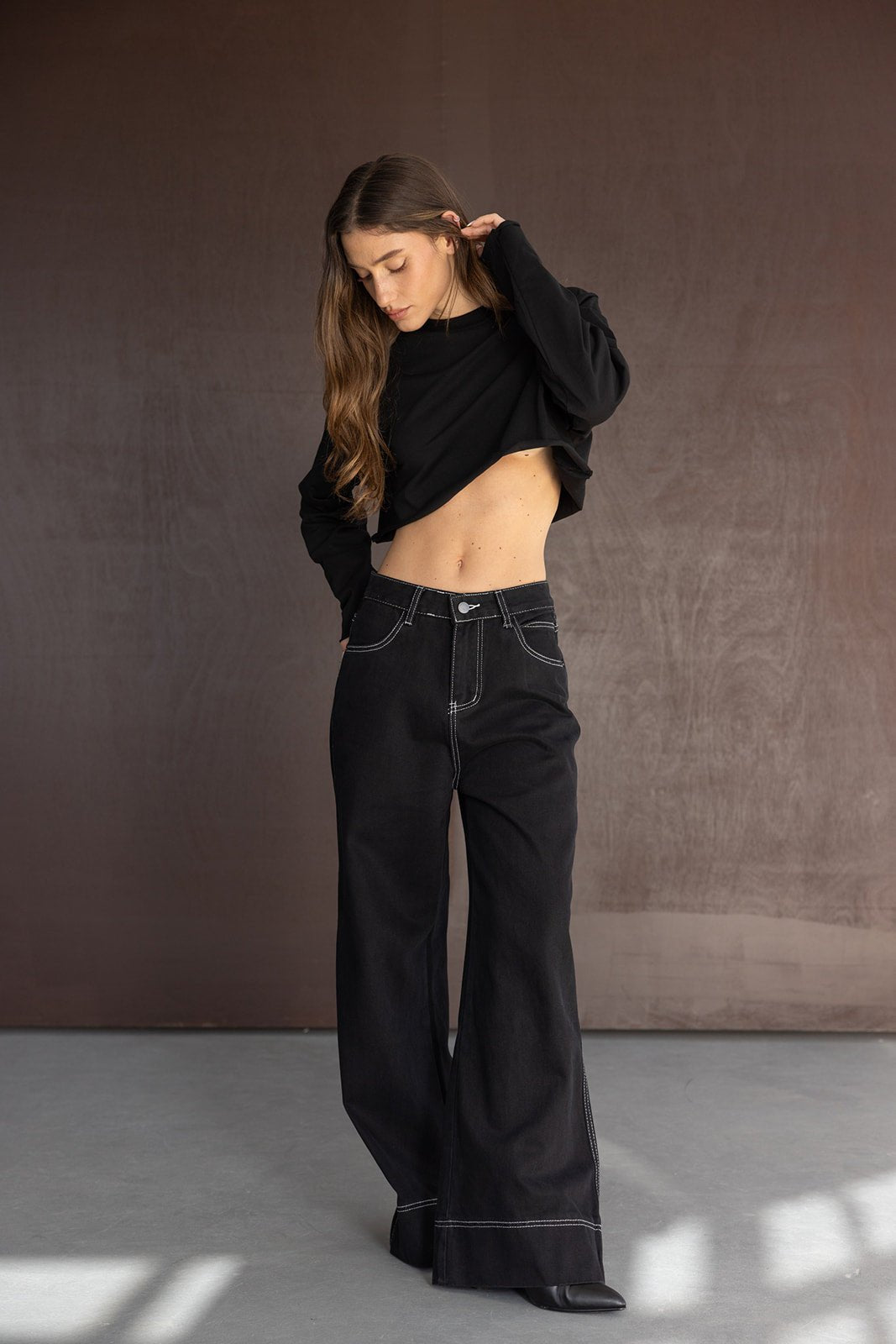 אישה לובשת חולצת קרופ שחורה ומכנסי ג'ינס שחורים בגזרה רחבה, אופנת רחוב לנשים צעירות