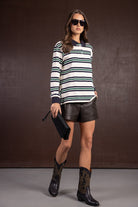 דוגמנית עם חולצת פסים ארוכה, מכנסי דמוי עור קצרים, מגפיים שחורים ומשקפי שמש אופנתיים