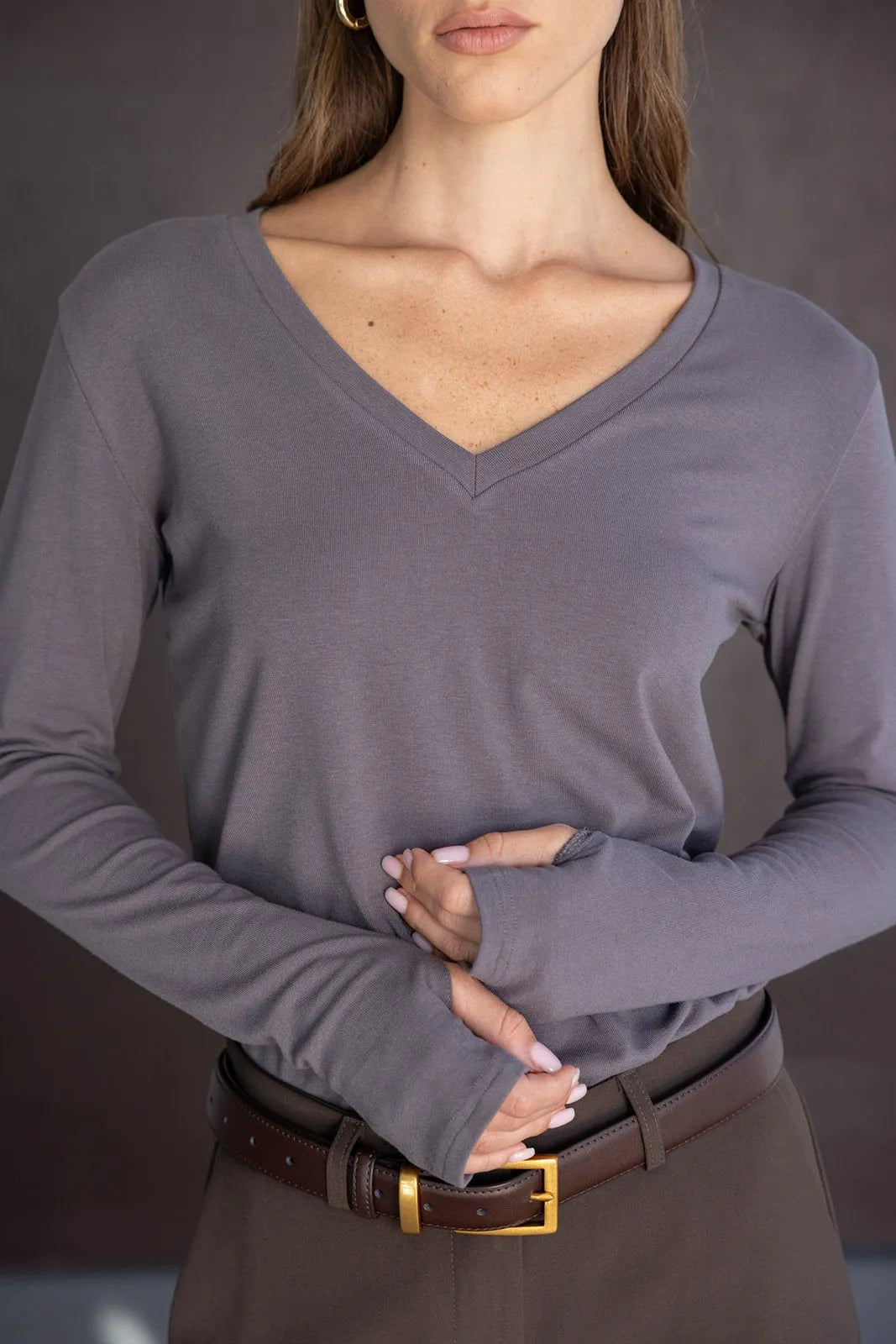 חולצת נשים ארוכת שרוולים עם מחשוף וי בגוון אפור שיקי, משולבת עם מכנסיים חגורה חומה