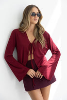 אישה צעירה עם משקפי שמש, לובשת חצאית מיני ובגד עליון בורדו בעיצוב אופנתי עם שרוכים