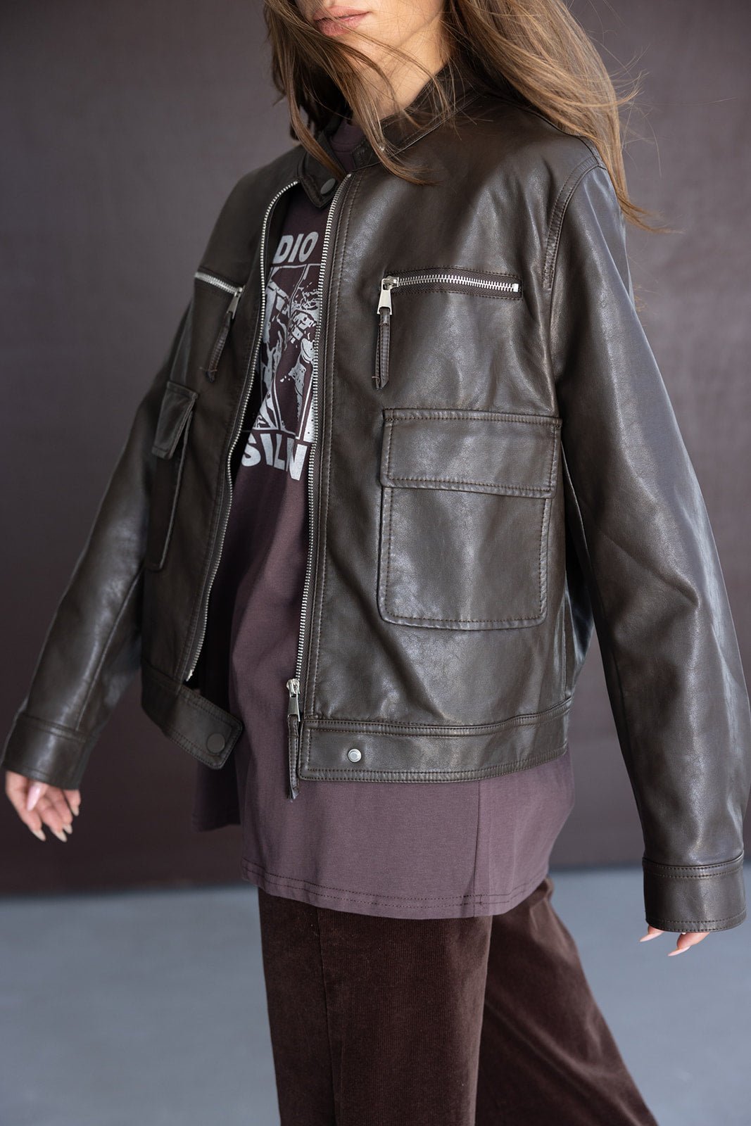 אישה לובשת ז'קט עור חום עם כיסים קדמיים, חולצה כהה ומכנסיים רחבים, אופנת חורף לנשים