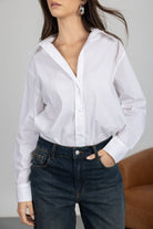 אישה לובשת חולצה לבנה מכופתרת ומכנסי ג'ינס בגזרה גבוהה, אופנת נשים קלאסית