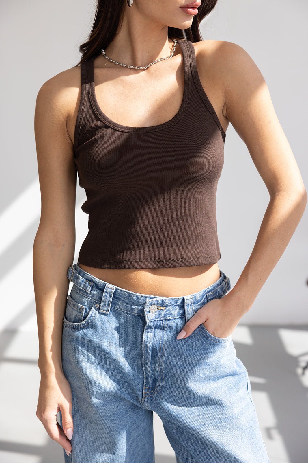 דוגמנית לובשת גופיית קיץ חומה עם כתפיות ומכנסי ג'ינס בגזרה גבוהה, אופנת נשים צעירה