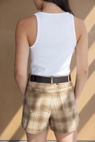 אישה עם גופיה לבנה ומכנסיים קצרים משובצים בגווני בז' חגורת עור, אופנת קיץ לנשים