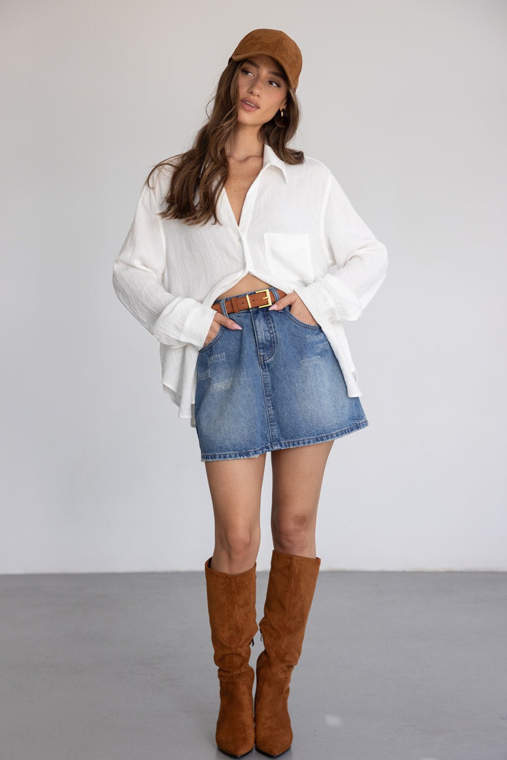 אופנת נשים: דוגמנית עם חצאית ג'ינס, חולצה לבנה, כובע חום ומגפיים גבוהים לחורף