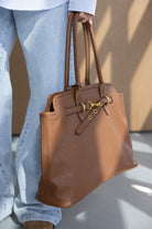 תיק יד גדול בצבע חום לנשים עם אבזמים זהובים, משולב עם ג'ינס וחולצה פסים