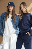 שתי נשים לובשות בגדי קז'ואל אופנתיים, אחת בסט אפור עם ג'קט ג'ינס וכובע, השנייה בסט כחול