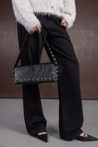 תיק צד שחור עם ניטים כסופים, מכנסיים שחורים רחבים, נעליים שחורות מחודדות