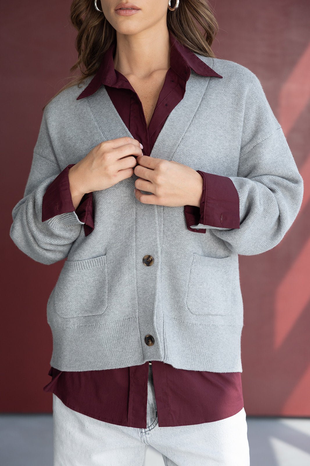 אישה לובשת סוודר אפור עם כפתורים מעל חולצה בורדו ואוזני חישוק, אופנת חורף לנשים