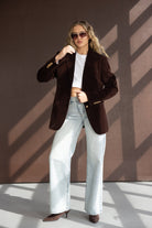 אישה צעירה עם ז'קט חום, ג'ינס רחב, חולצת קרופ לבנה ומשקפי שמש אופנתיים