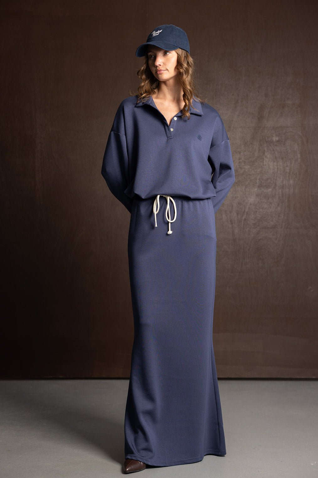 דוגמנית לובשת שמלת ספורט ארוכה בצבע כחול כהה עם שרוך במותן וכובע תואם, ביגוד אופנתי לנשים