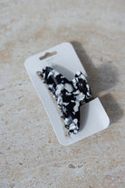 קליפס שיער טרנדי שחור עם דוגמת שיש לבנה, מונח על כרטיס קרטון לבן, לאביזרי שיער אופנתיים