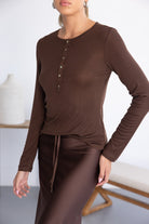 דוגמנית לובשת חולצת בייסיק חום כהה עם כפתורים וחצאית חומה, אופנת נשים טרנדית