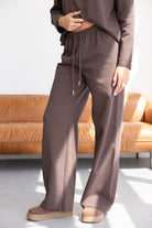 סט טרנינג חום לנשים עם מכנס רחב ונעליים שטוחות, על רקע ספה מעוצבת