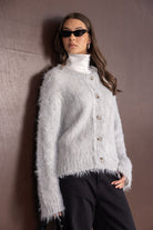 צעירה עם סוודר פרוותי אפור, גולף לבן, משקפי שמש שחורות ומכנס שחור – אופנת נשים חורף