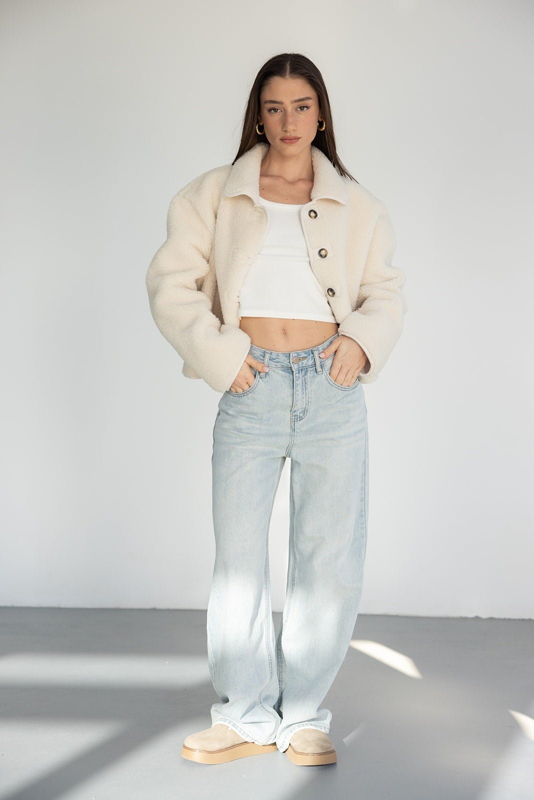 אישה עם מעיל פלאפי לבן, גופייה לבנה ומכנסי ג'ינס רחבים, אופנה לנשים צעירות