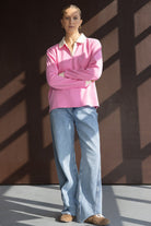 אישה לובשת סווטשירט ורוד עם צווארון לבן, מכנסי ג'ינס רחבים ונעלי סניקרס חומות, מצולמת בסטודיו מואר