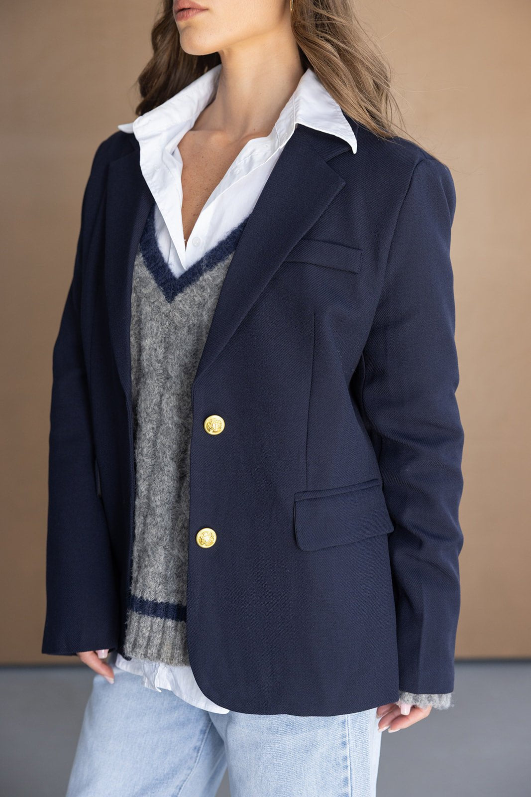 אישה עם בלייזר כחול קלאסי, סוודר אפור, חולצה לבנה וג'ינס אופנתי