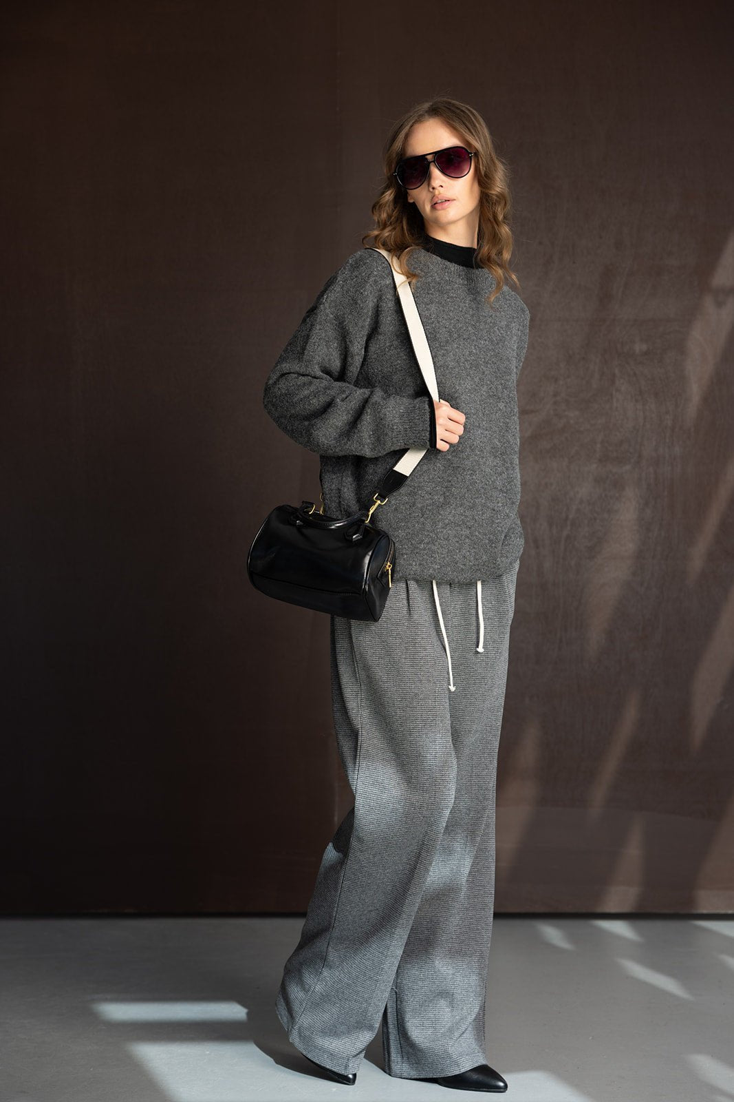 אישה לבושה בסט טרנינג אפור, משקפי שמש ותיק שחור, אופנת נשים מודרנית