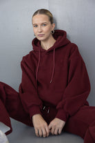 דוגמנית יושבת עם סווטשירט בורדו קפוצ'ון טרנדי ואופנתי לנשים