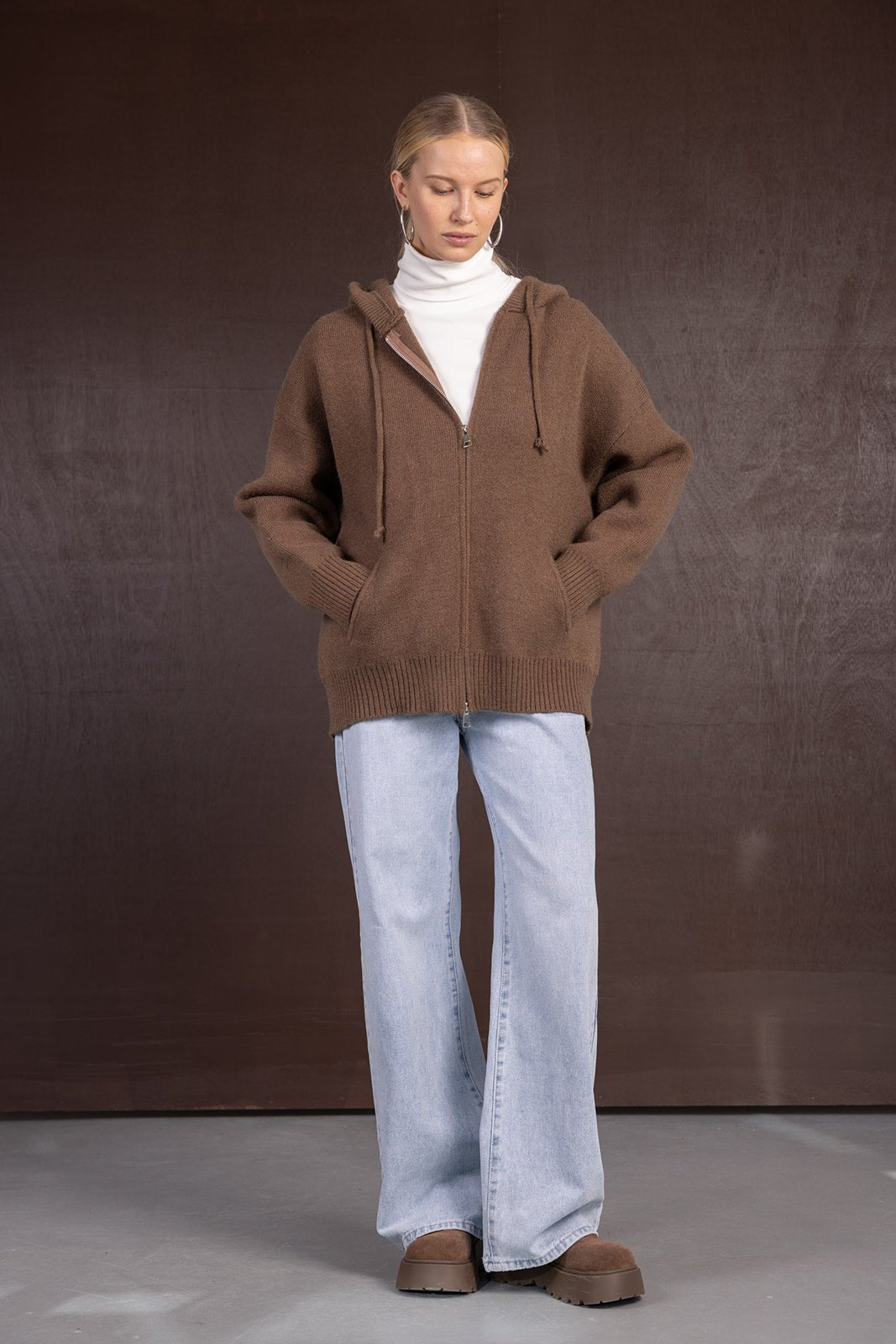 אישה עם סווטשרט חום עם רוכסן, גולף לבן, ג'ינס רחב ונעלי חורף חומות, אופנת חורף לנשים