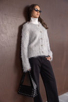 דוגמנית לובשת סוודר אפור פרוותי עם כפתורים, מכנסיים שחורים ותיק צד שחור, מראה אופנתי קז'ואל לנשים