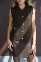 אישה לובשת וסט סרוג חום עם כפתורים זהובים וחצאית חומה, אופנה לנשים צעירות