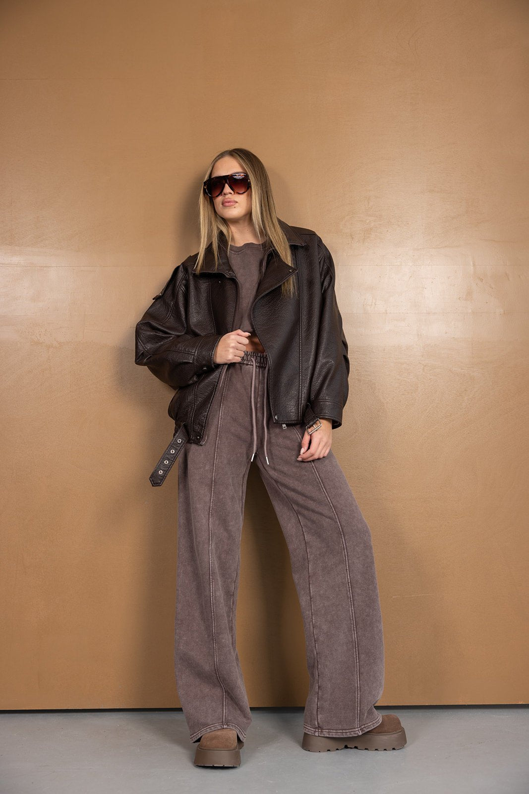 אישה עם מעיל עור חום, מכנסיים רחבים וחולצת טריקו אופנתית, לוק חורפי עדכני לנשים