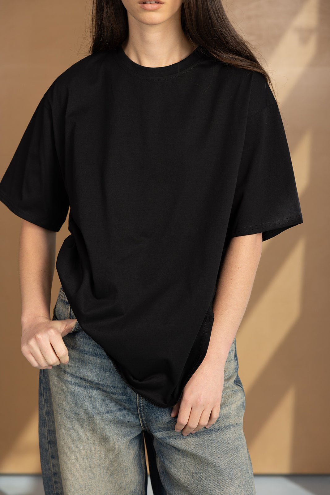 חולצת טי שירט שחורה לנשים, גזרת אוברסייז, עם מכנסי ג'ינס אופנתיים רקע חום