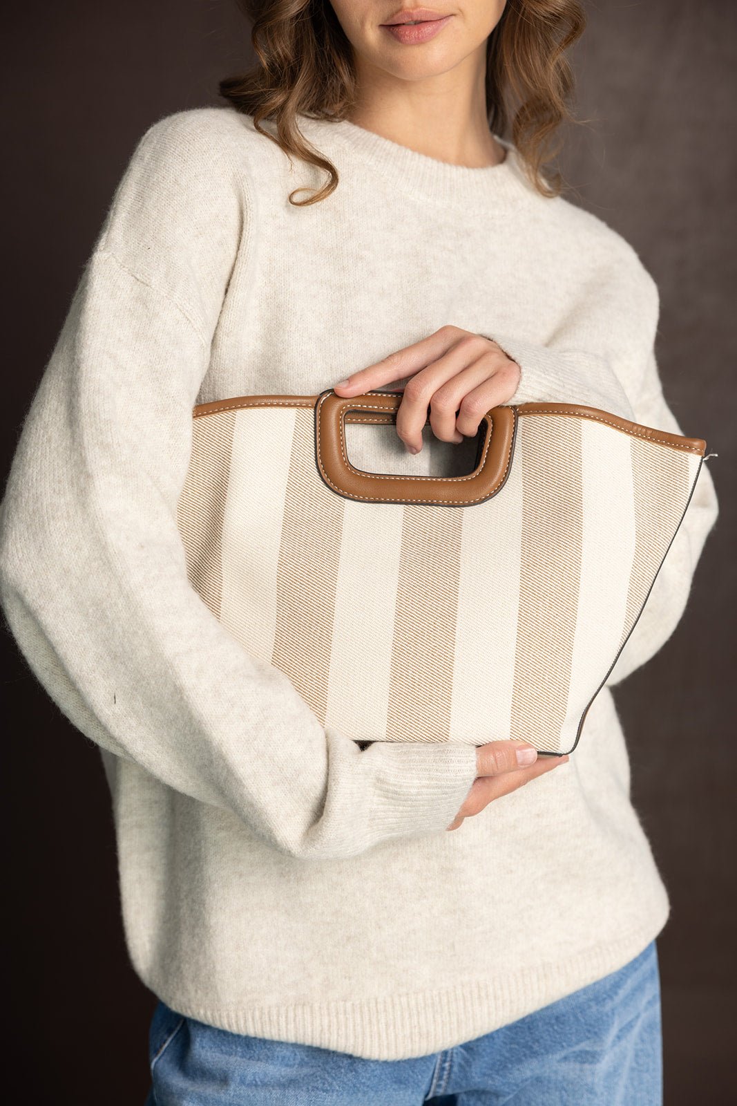 אישה בלבוש חורפי מחזיקה תיק יד מחויט עם פסים בז' ולבן, אופנה לנשים