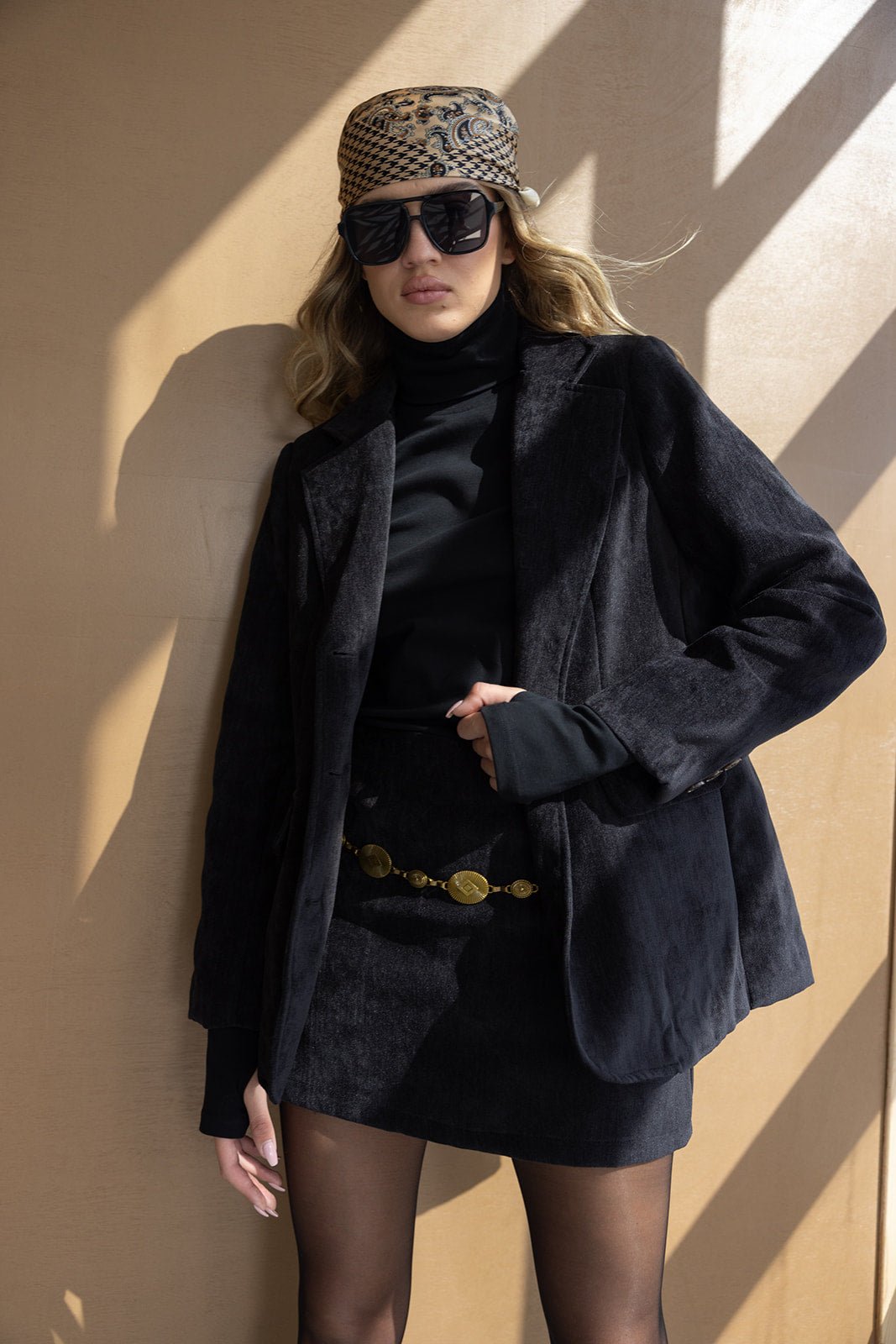 אישה עם ז'קט ומיני שחור, טופ גולף, צעיף מודפס, חגורת זהב ומשקפי שמש, אופנת נשים ישראלית