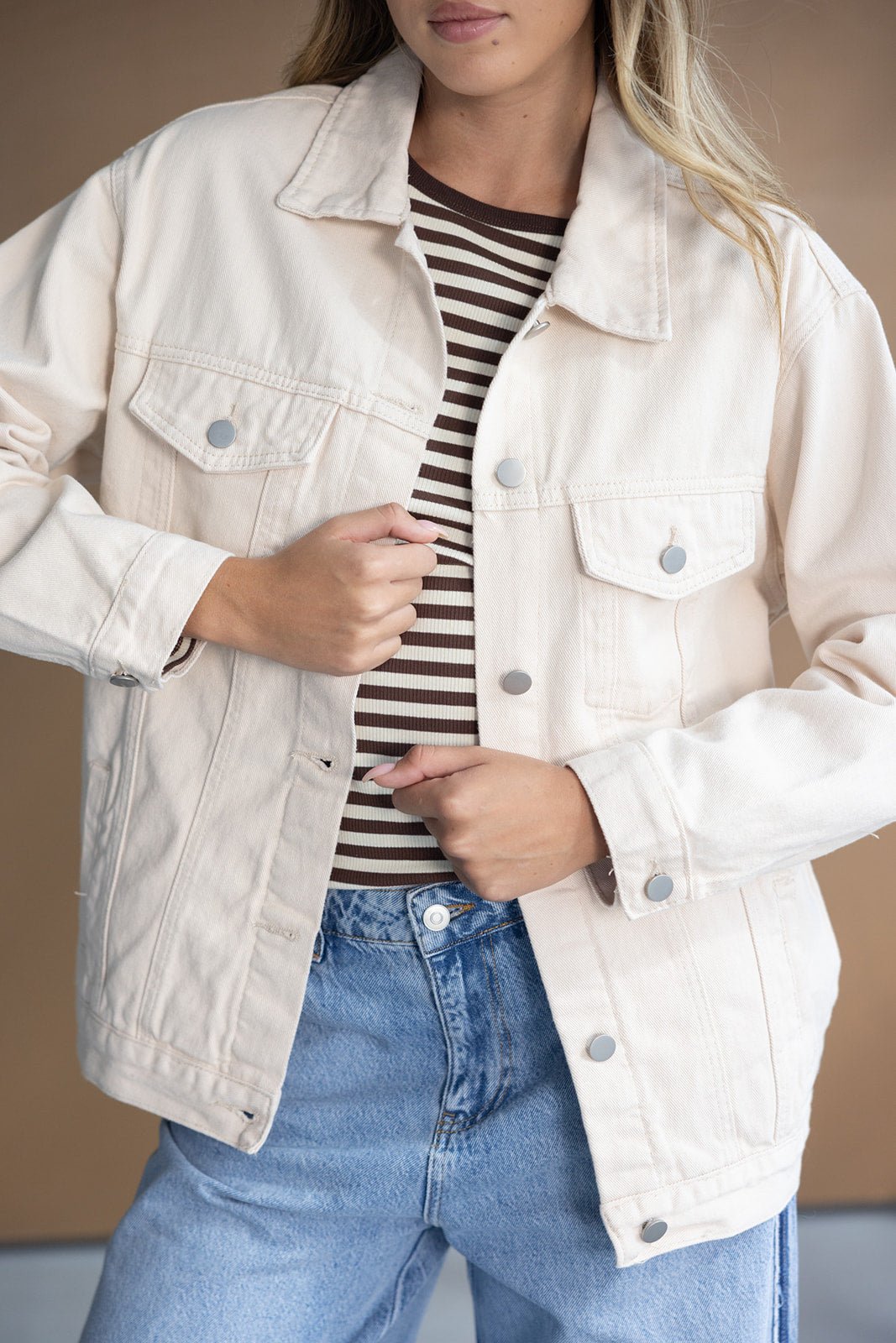 מעיל ג'ינס אופנתי לנשים בצבע בז', עם חולצת פסים חומה ומכנסי ג'ינס בהירים