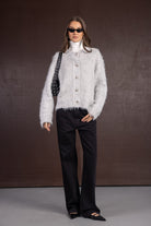 אישה עם סוודר פרוותי אפור, גולף לבן, מכנסיים שחורים ומשקפי שמש אופנתיים