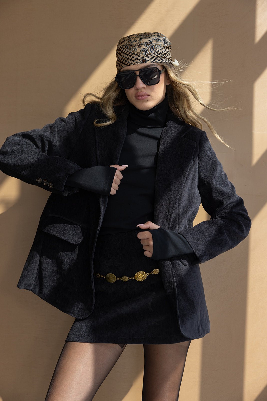 אישה עם חולצה שחורה, ז'קט שחור, חצאית מיני, צעיף מודפס ומשקפי שמש אופנתיים