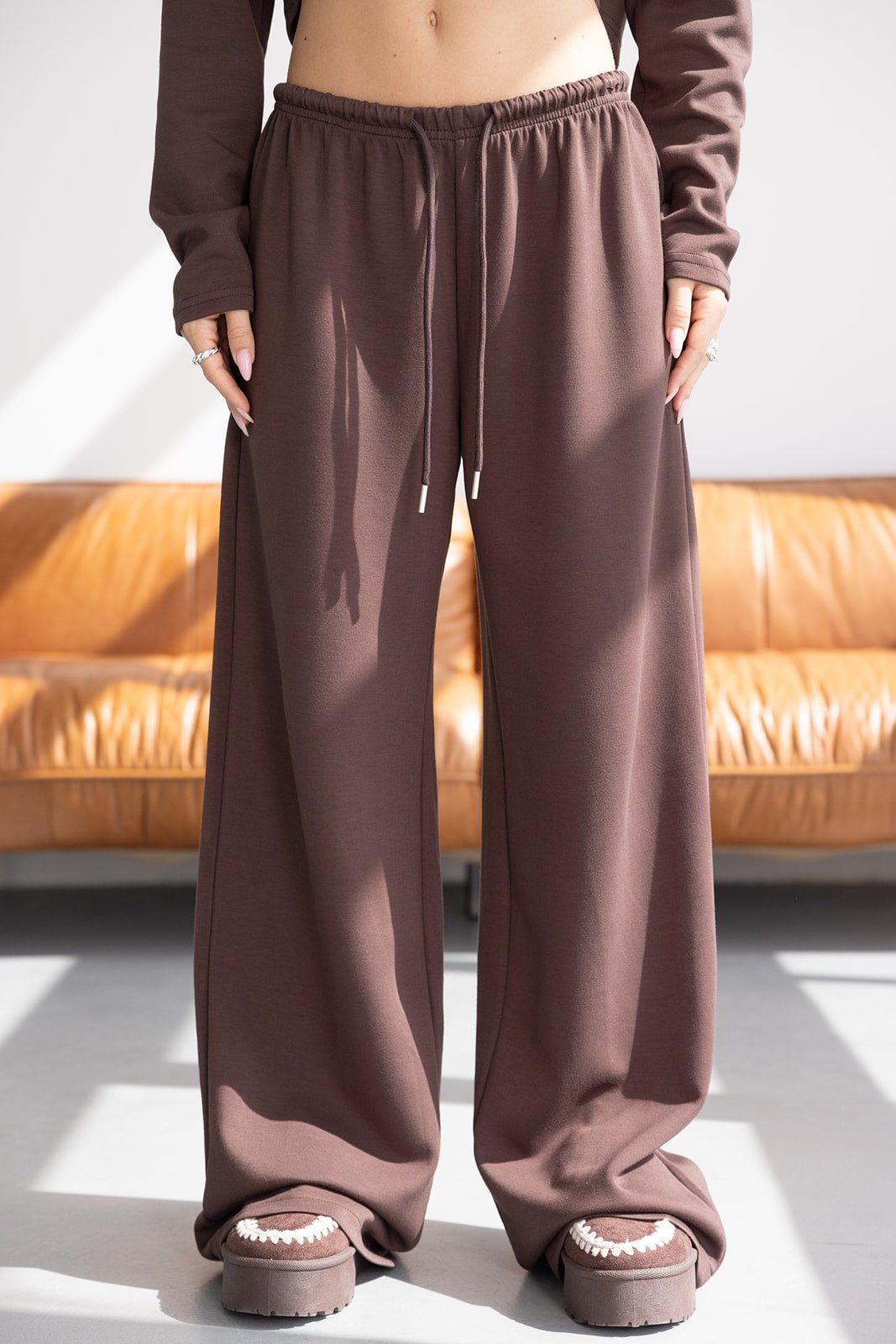 מכנסי טרנינג חום רחבים לנשים עם שרוך, סטייל אופנתי, צילום באור יום בסלון מודרני