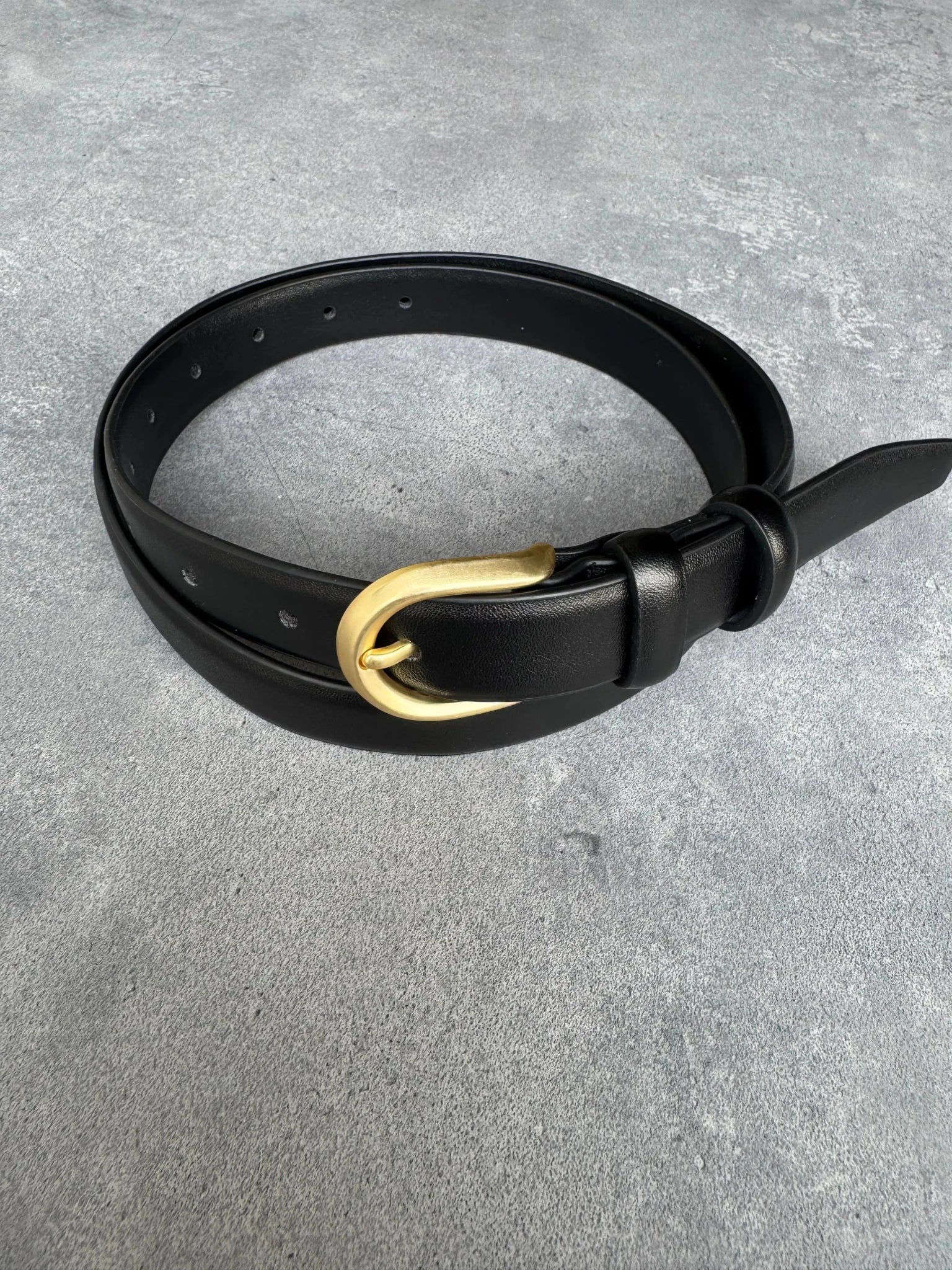 חגורת עור שחורה לאישה עם אבזם מתכת זהב, אופנה לנשים, מונחת על רקע בטון אפור