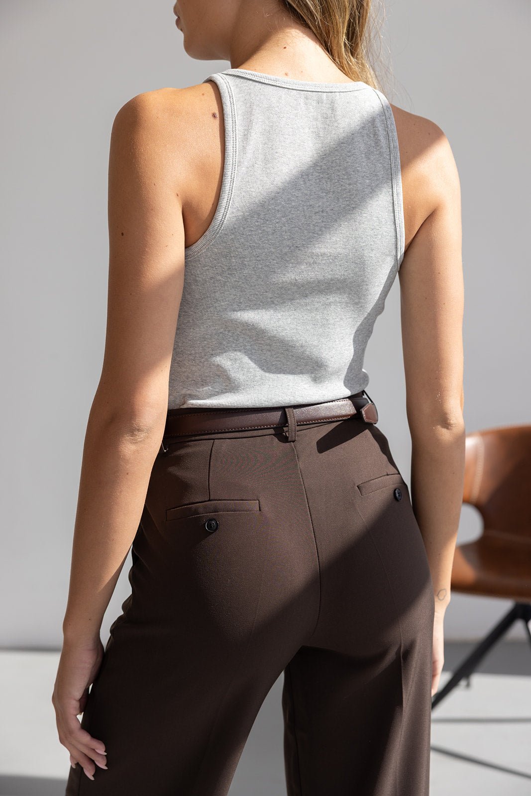 אישה עם גופיה אפורה ומכנסיים חומים מחויטים, מצולמת מאחור, אופנת נשים קיץ