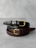 חגורות נשים בצבע שחור וחום עם אבזם זהב, דמוי עור תנין, על רקע אפור