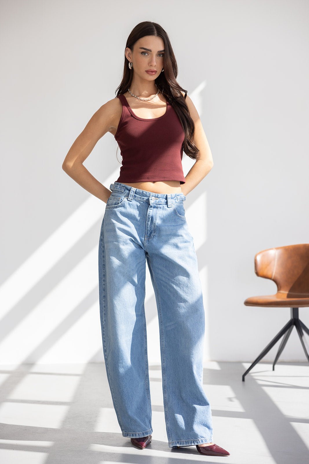 דוגמנית לובשת גופיה בורדו ומכנסי ג'ינס רחבים, אופנת נשים צעירה ואורבנית, רקע סטודיו מואר