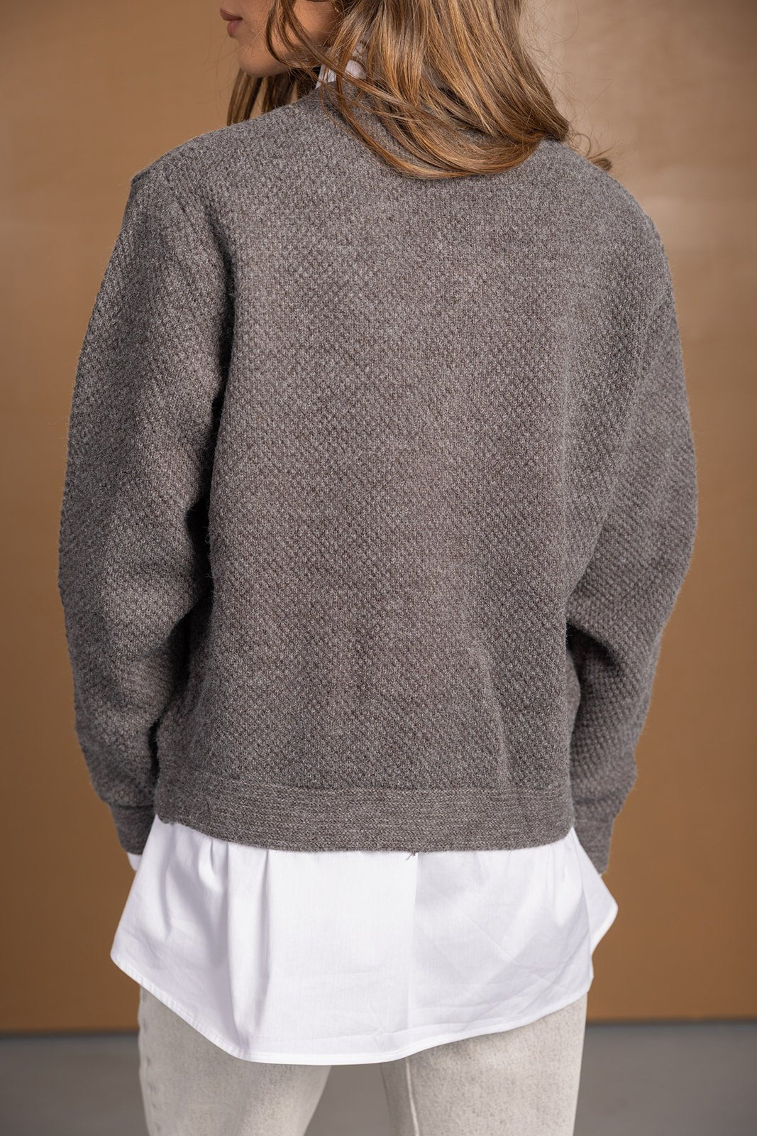 אישה לובשת סוודר אפור מרקם בשכבה עליונה מעל חולצה לבנה ומכנסיים בהירים, אופנה לנשים