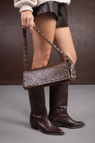 מגפיים חומים גבוהים, תיק עור חום עם ניטים, שורטס שחור וסוודר בז' לאופנת נשים