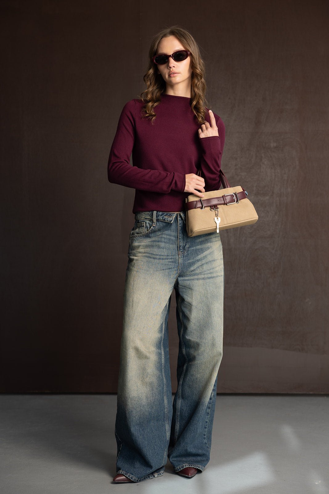 אישה עם חולצה בורדו, ג'ינס רחבים ומשקפי שמש, מחזיקה תיק אופנתי בסגנון קז'ואל