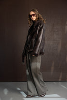 אישה עם מעיל עור חום, מכנסיים רחבים ומשקפי שמש אופנתיים, סטייל חורפי אלגנטי לנשים