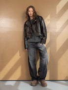 דוגמנית לובשת ג'קט עור שחור, סוודר אפור, ג'ינס רחב ונעלי פלטפורמה חומות, לוק קז'ואל אופנתי לחורף