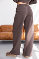 מכנסיים רחבים חומות לנשים, גומי במותן, ליד ספה מעור בסלון מואר