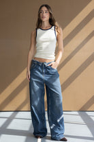 דוגמנית לובשת גופיית סריג לבנה עם קצוות כהים ומכנסי ג'ינס רחבים, אופנת נשים צעירה