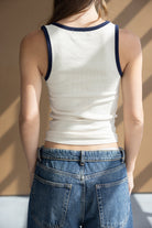 אישה לובשת גופיה לבנה עם שוליים כחולים ומכנסי ג'ינס אופנתיים, מצולמת מאחור